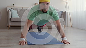 Tracking shot of overweight man practicing push ups at home, hardly exercising on floor, slow motion