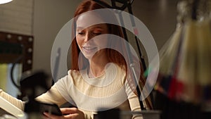 Tracking shot of smiling young woman client using browsing smartphone during manicure procedure in beautician salon.