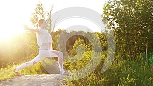 Tracking shot of woman practicing yoga and performing Warrior Pose outside in park evening.