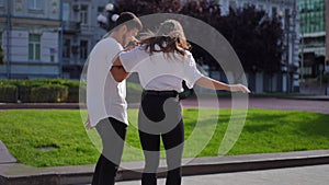 Tracking shot of young man holding hand of woman riding skateboard on city street smiling. Happy carefree Caucasian