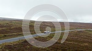 Tracking of single vintage convertible car with textile roof driving on road in countryside on cloudy day. Ireland