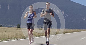 Tracking slow motion shot of sportive couple jogging outdoors in the morning, trail running experience in nature