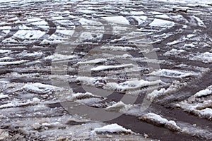 Tracks of car tires on melting snow on asphalt of the road