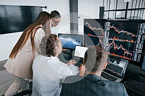 Tracks the graphs. Team of stockbrokers works in modern office with many display screens