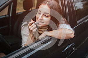 Tractive woman apply pink lipstick in front of rearview mirror in car. Close up Hand. Autumn concept. Autumn forest