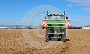 Tractor with an agricultural sprayer machine, spreads fertilizer on freshly plowed field in first spring