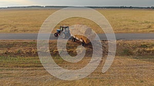 Tractor with bales of straw in the trailer goes hard from the field to the road