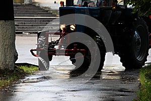 Tractor with a barrel on a trailer pours water over the city sidewalks, streams of water flow down to the ground