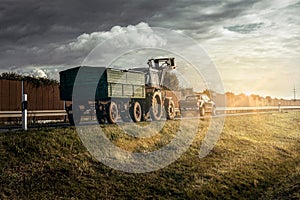 tractor behind a car truck on a country road in bright sun with sunbeams and gloomy sky