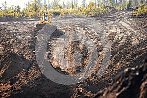 Tractor bulldozer removes top layer of fertile soil overburden forest, grass, harvesting site for open mine. Concept photo