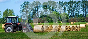 Tractor carrying hay bale rolls and collecting them on a field.