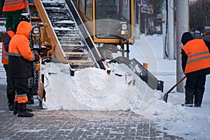 Tractor cleaning the road from the snow. Excavator cleans the streets of large amounts of snow in city. Workers sweep