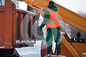 Tractor cleaning the road from the snow. Excavator cleans the streets of large amounts of snow in city. Workers sweep