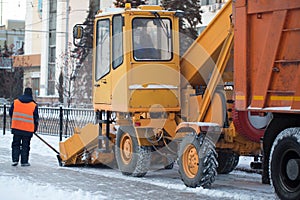 Tractor cleaning the road from the snow. Excavator cleans the streets of large amounts of snow in city. Workers sweep