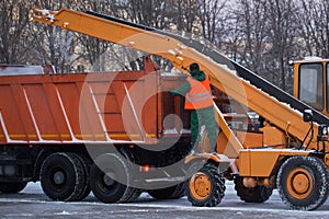 Tractor cleaning the road from the snow. Excavator cleans the streets of large amounts of snow in city. Workers sweep