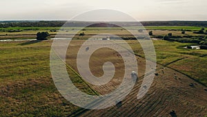 Tractor collecting hay bales. Aerial footage of farmer & haystacks