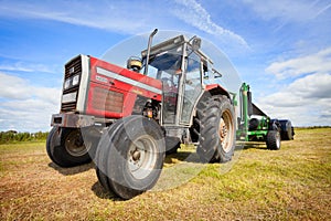 Tractor collecting a roll of haystack in the field