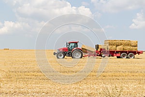 Tractor collecting straw bales during harvesting in the field at nice blue sunny day