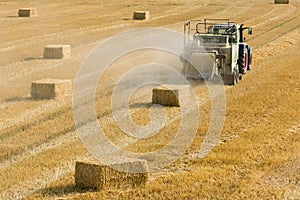 Tractor collects dry hay on the farm field and makes hay bales