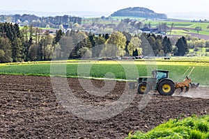 A tractor cultivates a plowed field in the spring