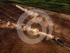 Tractor cultivating field, kicking up rocks and dust in early mo