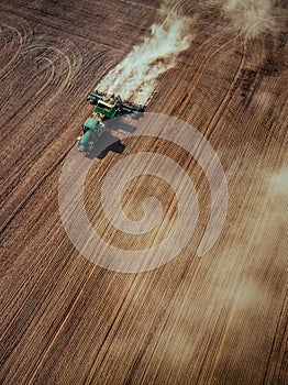 Tractor cultivating field, kicking up rocks and dust in early mo