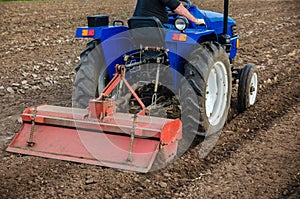 The tractor is cultivating the soil in the farm field. Freeing milling earth ground from old crops. Softening and improving soil