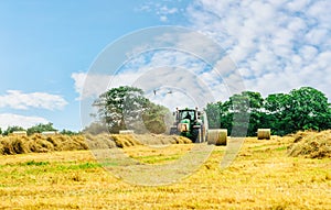 Tractor cutting hay in summer time against blue cloudy sky,  haystacks on the field