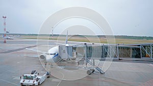 The tractor drawing near the airplane before flying and aircraft technician checking detaching of the airbridge from the