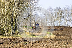 Tractor drives on a gravel road by a plowed field in springtime