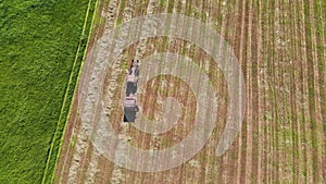 A tractor is driving and collecting the mown hay into bales, aerial view.