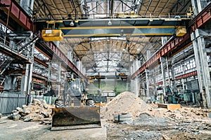 Tractor or excavator with bucket in large industrial workshop at factory, heavy industry concept