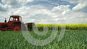 Tractor and farmer in the agricultural wheat and rapeseed fields and dramatic clouds