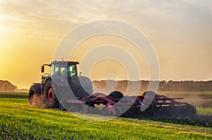 tractor in the field under sunset light, tillage in spring, preparation for sowing