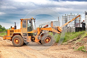 A tractor or forklift is stationary on the side of a dusty rural road, surrounded by fields and under a clear sky