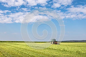 Tractor in green field under blue sky with clouds