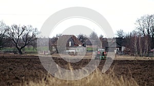 Tractor handles the field with a disk harrow against the background of the village buildings