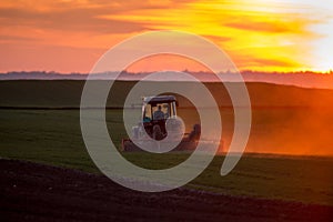 Tractor harrowing field at sunset