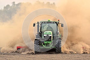 The tractor harrows the field in a huge dust cloud.