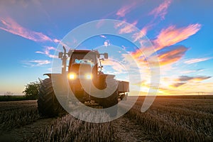 Tractor on harvested grain field during dusk