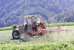 Tractor with hay tedder working on a mountain field