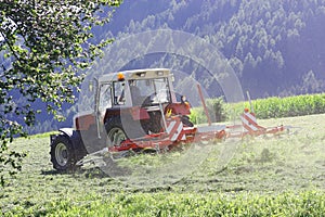 Tractor with hay tedder working on a mountain field