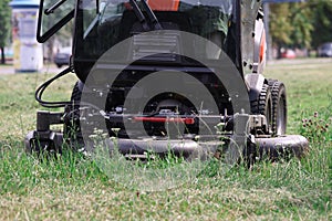 Tractor lawn mower mowing grass in park closeup