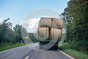 Tractor loaded with several straw bales drives over a country road