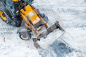 Tractor loader machine uploading dirty snow into dump truck. Cleaning city street, removing snow and ice after heavy