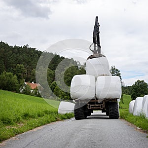 loading white grass rolls on country road in norway