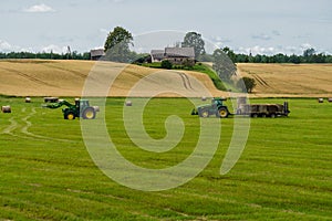 A tractor loads bales of hay onto a trailer from another tractor