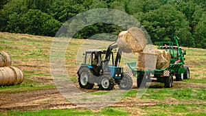 tractor loads round bales of straw on the trailer