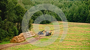 tractor loads round bales of straw on the trailer