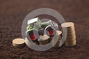 Tractor miniature with coins on fertile soil land